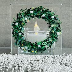 a candle surrounded by white balls and greenery on a glass block with water in the background