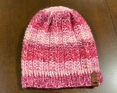 a pink and white knitted beanie sitting on top of a wooden table next to a button