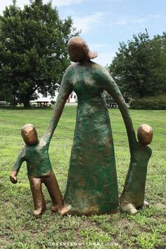 a statue of a woman and child holding hands in the grass with trees in the background