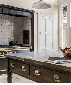 an old fashioned kitchen with marble counter tops and wooden cabinets, along with a bowl of fruit on the island