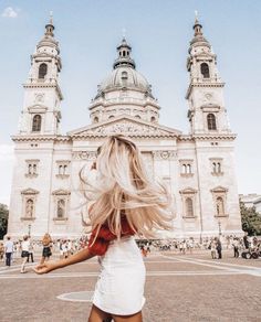 a woman is walking in front of a large building with two towers and a bell tower