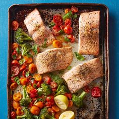 salmon, broccoli and tomatoes on a baking sheet with lemon wedges for garnish