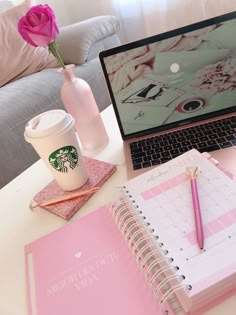 a desk with a laptop, coffee cup and pink notebook