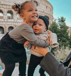 a woman holding a small child in front of the colossion, with one arm around her head