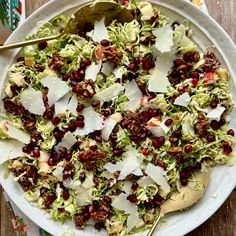 a white plate topped with lettuce and pomegranates next to a spoon