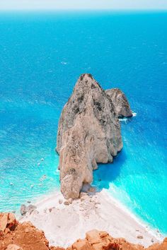 a large rock sitting on top of a sandy beach next to the blue water in the ocean