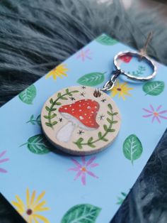 a wooden keychain with a red mushroom on it's side and green leaves around the edges