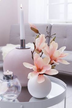 a vase filled with flowers next to a candle on top of a glass table in front of a couch