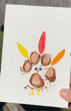 a hand holding up a paper with a turkey on it's face and leaves painted on it