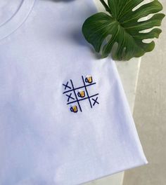 a white t - shirt with blue and yellow embroidered designs on it next to a plant