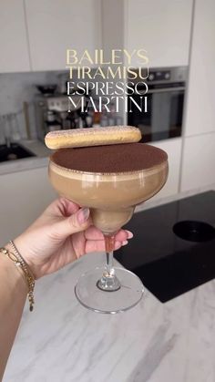 a person holding up a chocolate dessert in a wine glass with the words bailey's tramsu espresso martini on it