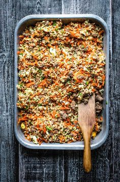 a casserole dish filled with carrots, ground beef and rice next to a wooden spoon