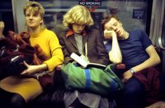 three people sitting on a subway train looking at something in their hand bags and reading