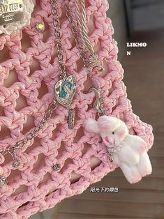 a pink crocheted purse with charms hanging from it's front and side