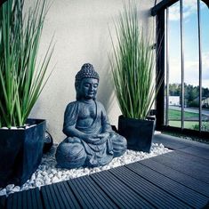 a buddha statue sitting on top of a wooden floor next to two planters filled with grass