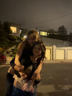 two women hugging each other in the middle of an empty parking lot at night time