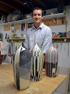 a man standing next to three vases on top of a wooden table in a room