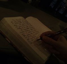 a person writing on an open book with a pen in their hand and the pages are lined up