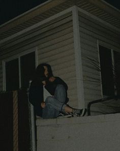 two people sitting on the ledge of a house at night with their arms around each other