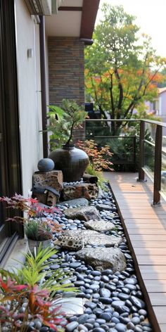 a small garden with rocks and plants on the side of a house's balcony