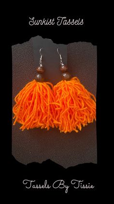 an orange tasseled pair of earrings on a black background with the words, sunset fasses