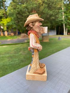 a wooden statue of a man drinking from a cup on top of a cement slab