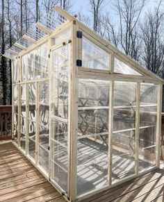 a small greenhouse with lots of windows on top of a wooden deck in front of trees