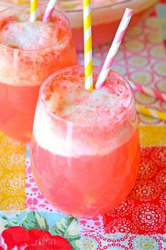 two glasses filled with ice and straws on top of a colorful table cloth next to plates