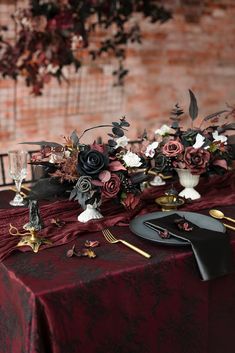 the table is set with black and red flowers, silverware, and wine glasses