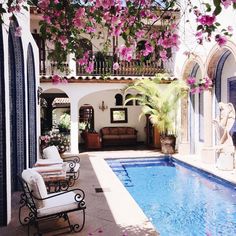 an outdoor swimming pool with chairs and flowers hanging from the ceiling over it's head