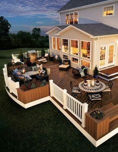 a deck with chairs and tables next to a large white house in the evening time