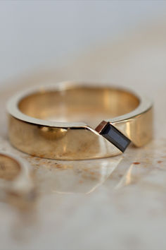 A gorgeous recent custom men's wedding band design, featuring a black moissanite baguette gemstone. The band is 14k yellow gold, and 5mm wide Mens Engagement Rings With Diamonds, Mens Wedding Rings Black And Gold, Engagement Rings Guys, Diamond Rings Mens For Men, Mens Wedding Bands Gold And Black, Diamond Wedding Ring For Men, Cool Engagement Rings For Men, Simple Engagement Rings For Men, Art Deco Mens Wedding Band