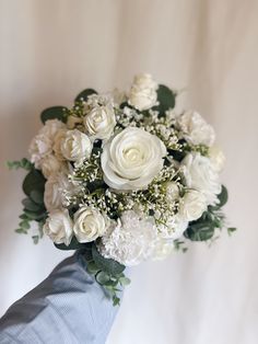 a bridal bouquet with white roses and greenery in it is being held by someone's hand