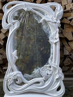 an ornate white mirror sitting on top of a pile of wood next to a pile of logs