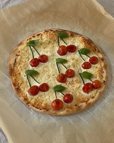 a pizza with cherry tomatoes and basil on it sitting on wax paper, ready to be eaten