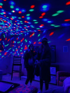 two people standing in a room with colorful lights on the ceiling