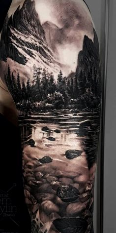 a man's arm with an image of mountains and trees on the water in it