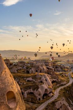 many hot air balloons are flying in the sky above some rocks and dirt roads, with mountains in the background