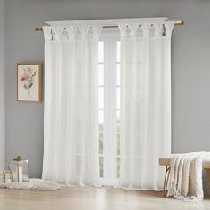 a white curtain hanging on the side of a window next to a wooden table and chair