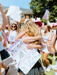 two women hugging each other in front of a group of girls holding signs and balloons