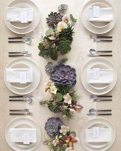 the table is set with white plates, silverware and succulents on it