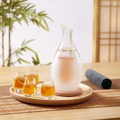 a pitcher and four glasses sitting on a wooden tray with a bamboo mat in the background