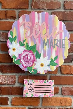 a wooden sign hanging on the side of a brick wall with flowers painted on it