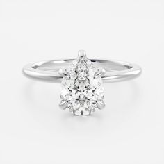 a pear shaped diamond engagement ring on a white background, with the center stone set in 18k white gold