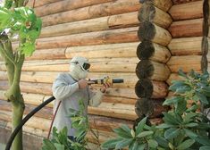 a man in a protective suit is using a power drill to cut down logs on the side of a log house