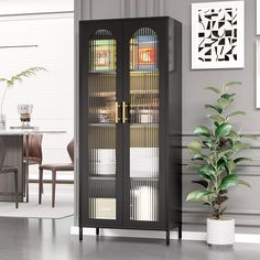 a black cabinet with glass doors in the middle of a room next to a potted plant