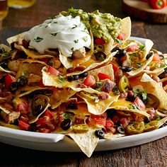 a plate full of nachos with sour cream on top and salsa in the middle