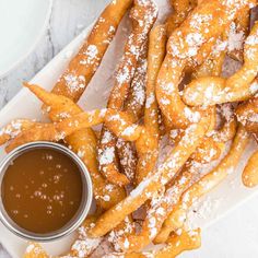 some churros and dipping sauce on a white plate with powdered sugar sprinkled on them