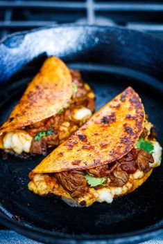 two quesadillas sitting on top of a skillet covered in meat and cheese