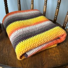 a multicolored knitted blanket sitting on top of a wooden chair next to a wood table